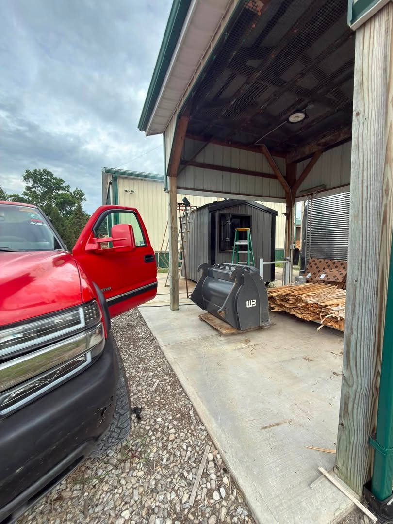 An excavator bucket under a shop lean-to next to the service pickup